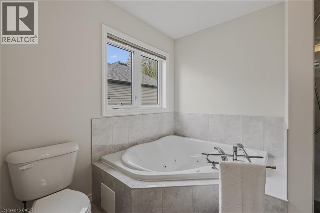 Bathroom featuring a corner jetted soaking tub with tile surround, a window with horizontal blinds, and a white toilet - 249 Woodway Trail, Simcoe, ON