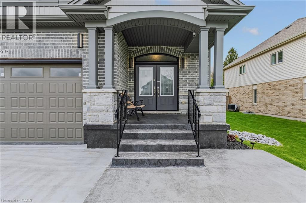 Stately brick and stone exterior featuring a covered entry, double front doors, an arched transom, and integrated exterior lighting - 249 Woodway Trail, Simcoe, ON