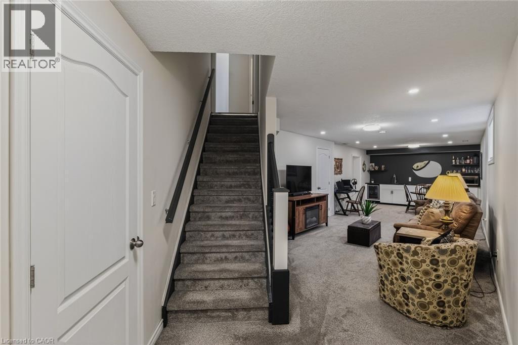 Finished lower level featuring carpeted flooring, recessed lighting, a built-in wet bar with shelving, a built-in entertainment console with an electric fireplace, and a white paneled door - 249 Woodway Trail, Simcoe, ON