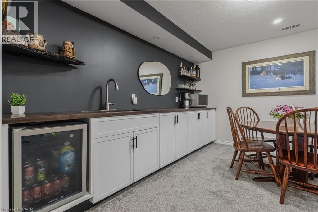 Custom bar area featuring rich wood-finish countertops, a stainless steel sink, and white cabinetry with matte black hardware - 249 Woodway Trail, Simcoe, ON