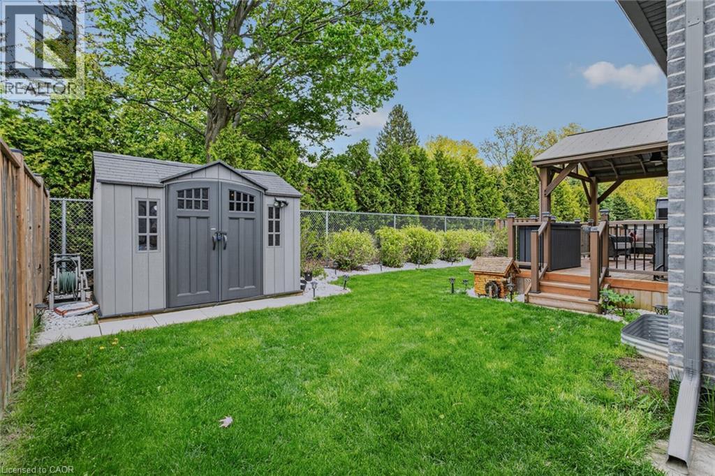 Expansive backyard featuring a manicured lawn, a detached storage shed, a wood-finish deck with a covered gazebo, mature perimeter trees, and a full fence surround - 249 Woodway Trail, Simcoe, ON