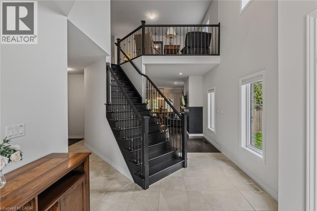 Two-story foyer featuring a dark wood staircase with wrought iron spindles, light tile flooring, white walls, and multiple windows - 249 Woodway Trail, Simcoe, ON