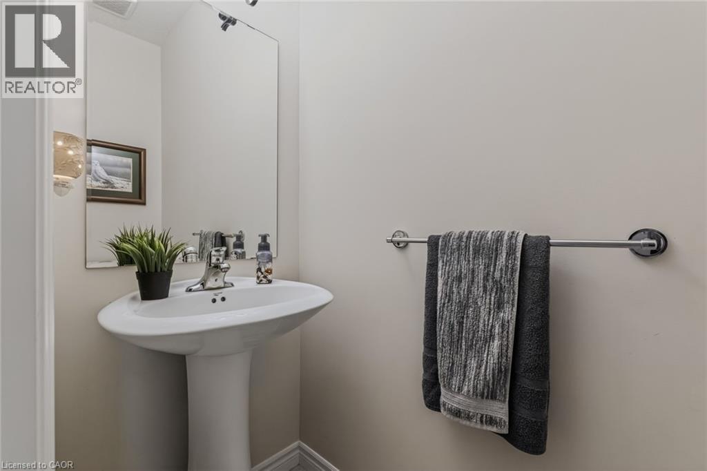 Pedestal sink with chrome faucet, large wall-mounted mirror, and a contemporary wall sconce providing illumination - 249 Woodway Trail, Simcoe, ON
