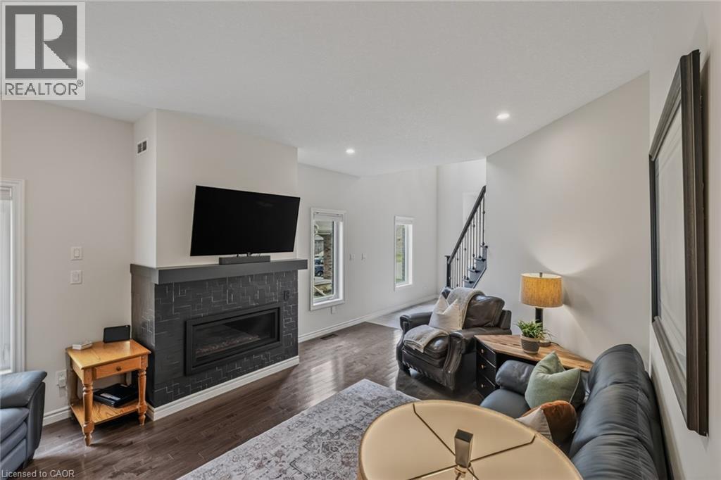 Living area featuring dark wood-finish flooring, a contemporary fireplace with dark tile surround and hearth, recessed lighting, and a staircase with dark risers and wrought iron balusters - 249 Woodway Trail, Simcoe, ON