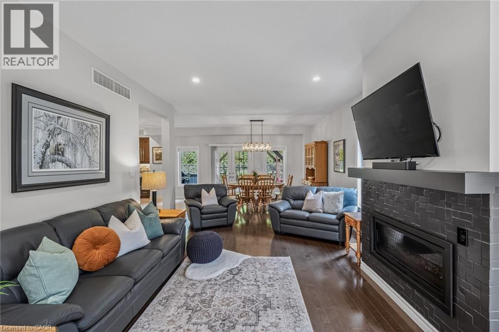Spacious living area featuring rich wood-finish flooring, a contemporary fireplace with stacked stone surround, recessed lighting, and a broad opening to the dining area - 249 Woodway Trail, Simcoe, ON