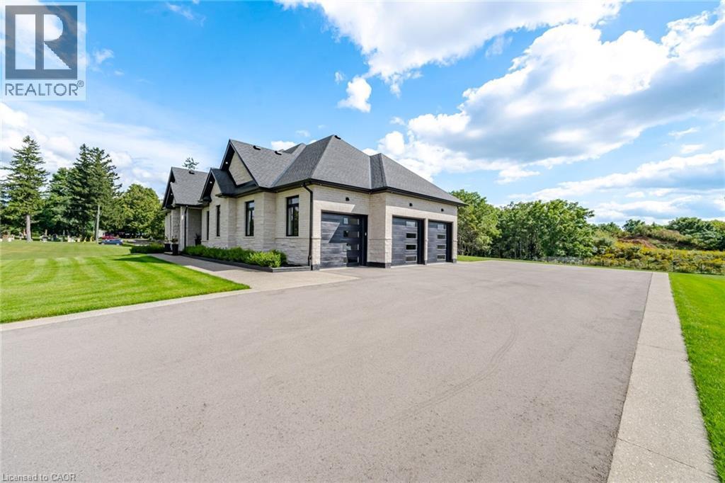 Stone exterior with dark framed windows, multi-car garage with black panel doors, dark shingle roof, and expansive asphalt driveway - 56 Augustus Street, Scotland, ON