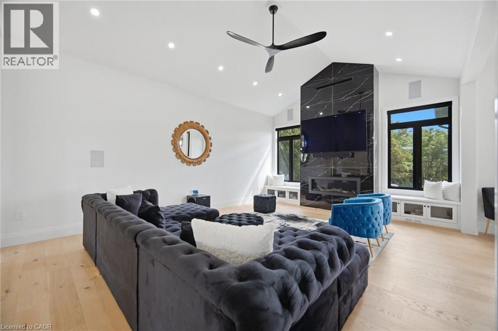 Vaulted ceiling with recessed lighting, wood-finish flooring, black marble-look fireplace surround, built-in window seating with storage, and large windows - 56 Augustus Street, Scotland, ON