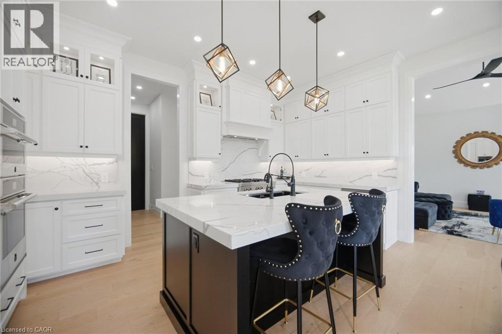 White cabinetry with black hardware, stone countertops with matching backsplash, central island with seating, stainless steel double oven, and light wood-finish flooring - 56 Augustus Street, Scotland, ON