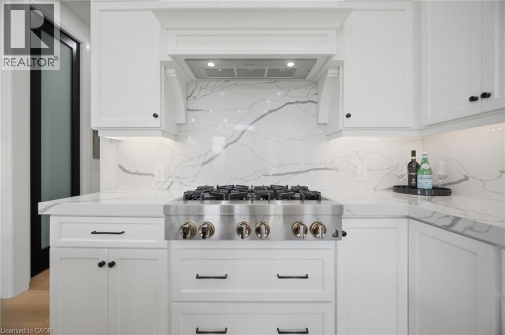 White cabinetry with dark hardware, stainless steel range, marble-finish backsplash, under-cabinet lighting, and light-toned flooring - 56 Augustus Street, Scotland, ON