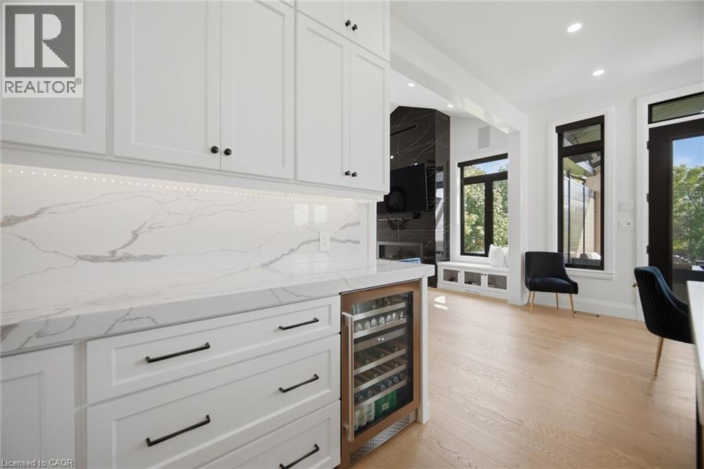 White cabinetry with black hardware, integrated beverage cooler, stone countertops, light wood-finish flooring, and black-framed windows - 56 Augustus Street, Scotland, ON