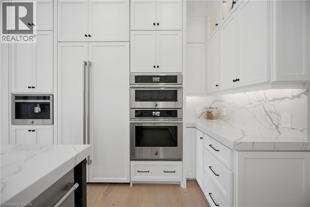 White cabinetry with black hardware, integrated stainless steel appliances, light wood-finish flooring, and white countertops extending into a matching backsplash - 56 Augustus Street, Scotland, ON