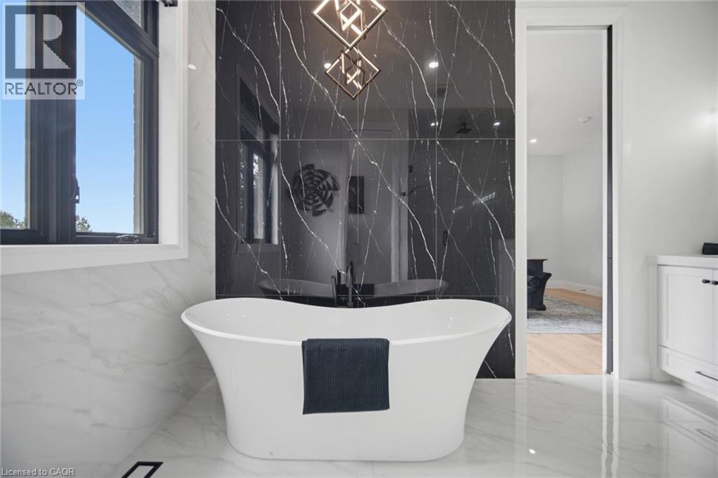 Freestanding soaking tub, black accent wall with white veining, white tile flooring, white wall tile, and black framed window - 56 Augustus Street, Scotland, ON