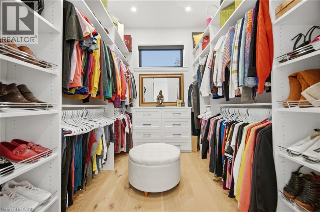Spacious walk-in closet featuring custom shelving, integrated hanging rods, a built-in chest of drawers, wood-finish flooring, and a transom window - 56 Augustus Street, Scotland, ON