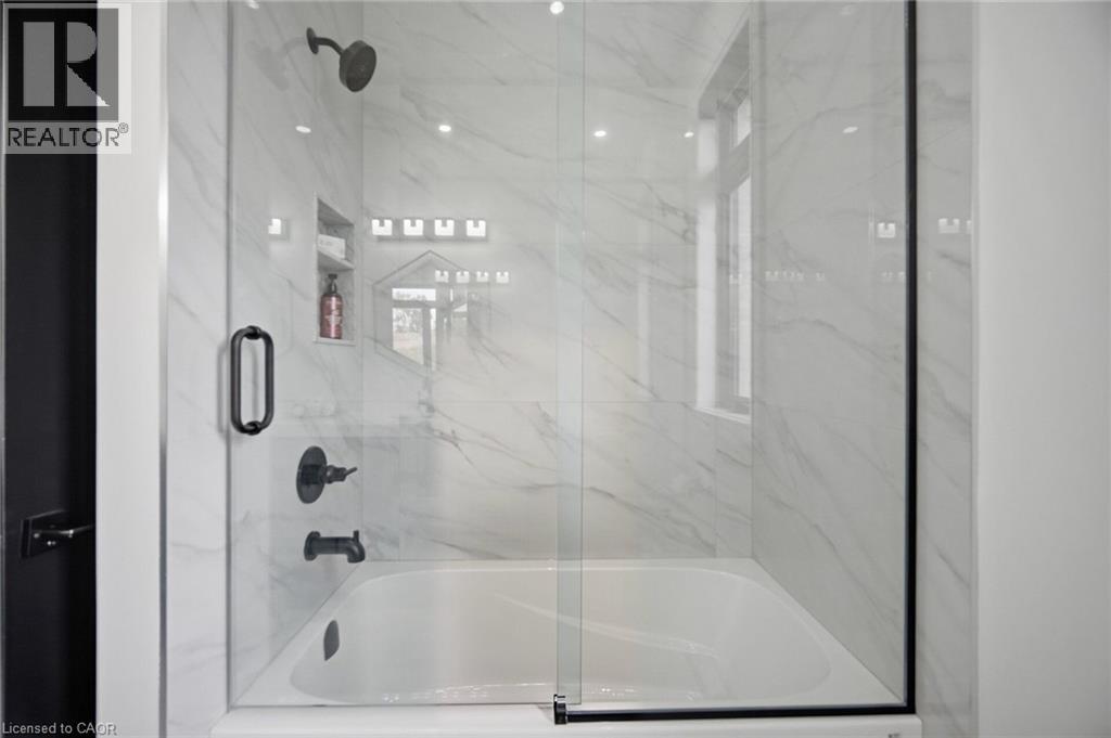Bathtub and shower combination featuring a glass enclosure, a tiled surround with a built-in niche, and matte black fixtures - 56 Augustus Street, Scotland, ON