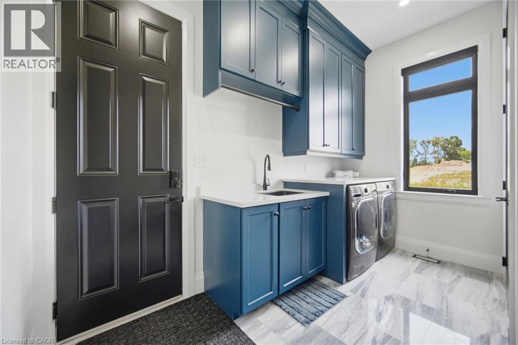 White-finish walls complementing the blue cabinetry, a sink with a black faucet, and large-format tile flooring - 56 Augustus Street, Scotland, ON
