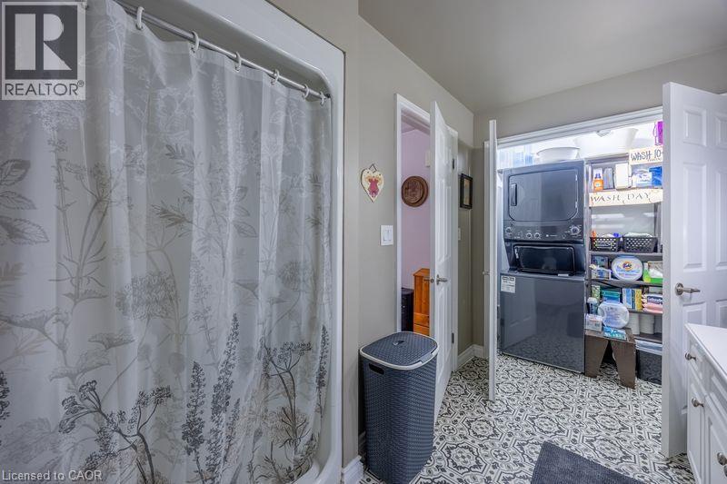 Built-in laundry closet with stacked washer and dryer, patterned floor tile, and white cabinetry with drawer pulls - 123 Mill Street, Delhi, ON