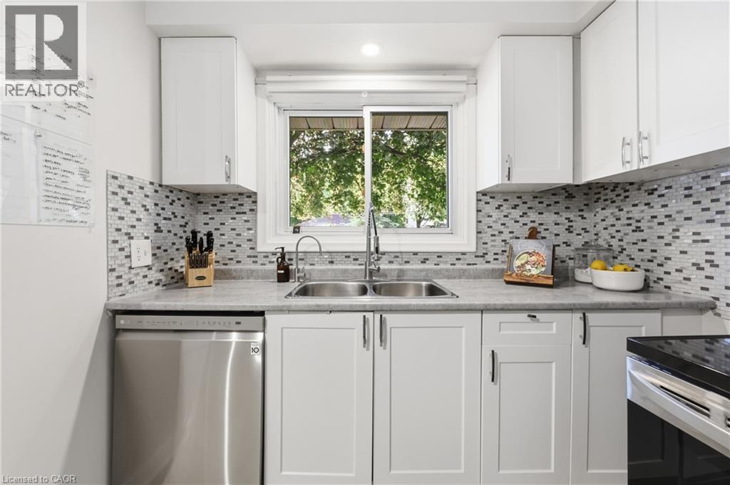 Kitchen featuring white shaker cabinetry, stainless steel dishwasher, dual basin undermount sink with gooseneck faucet, light-toned countertop, and mosaic tile backsplash - 312 Upper Paradise Road, Hamilton, ON