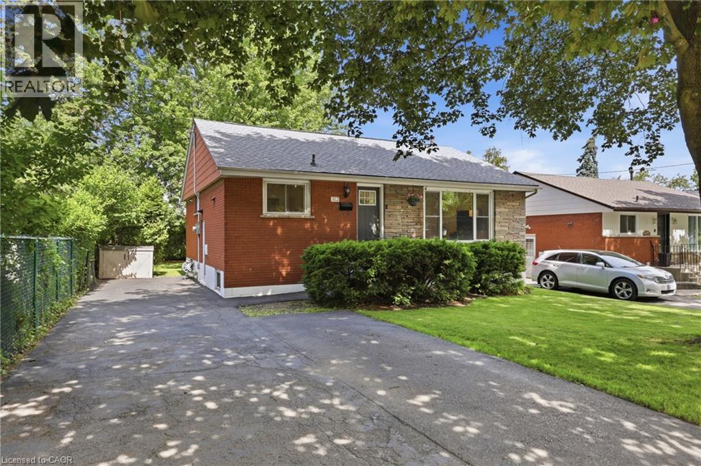Red brick exterior with stone facade accents, mature front yard landscaping, paved driveway, and chain-link fence - 312 Upper Paradise Road, Hamilton, ON