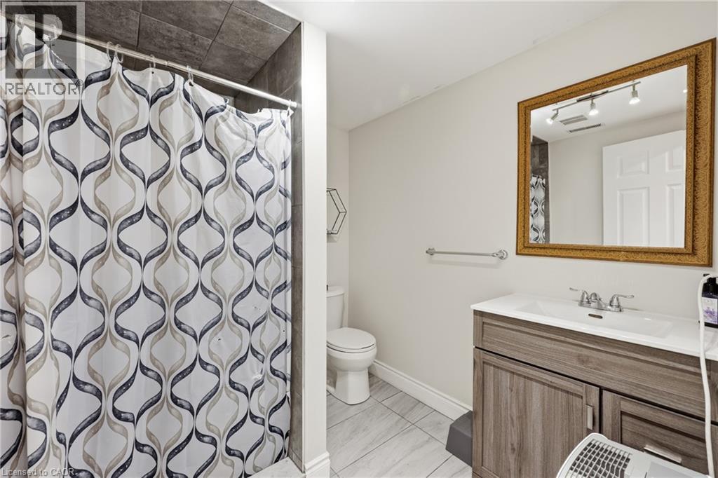 Bathroom featuring a vanity with wood-finish cabinetry, a white countertop with an integrated sink, a large framed mirror, and a tiled shower surround - 312 Upper Paradise Road, Hamilton, ON