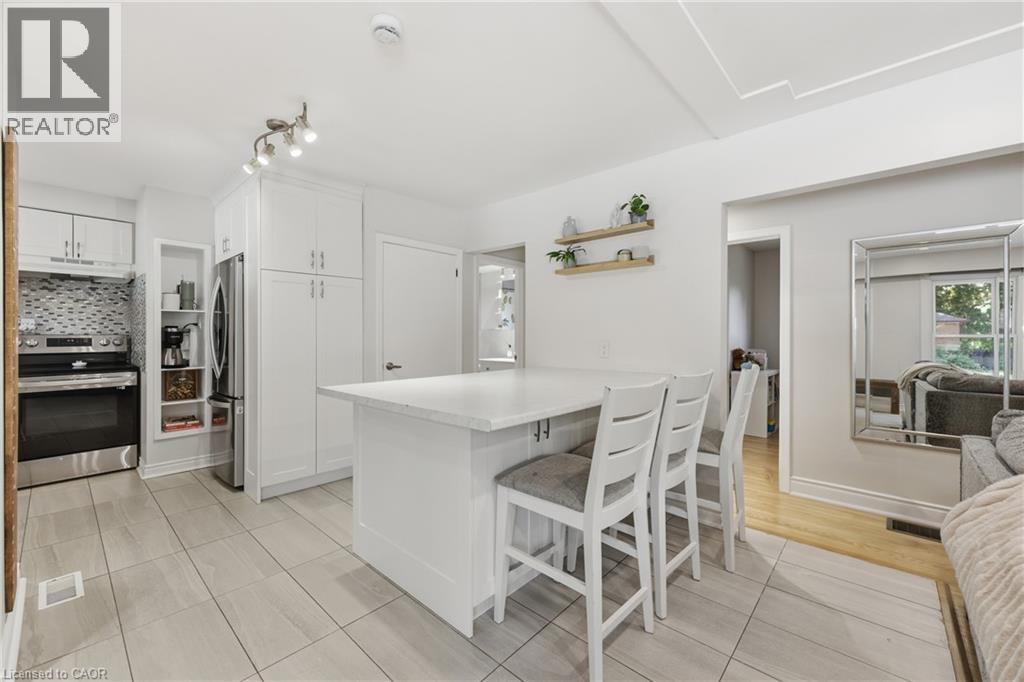 White shaker cabinetry, stainless steel appliances, tile flooring, kitchen island with seating, and decorative wall shelving - 312 Upper Paradise Road, Hamilton, ON