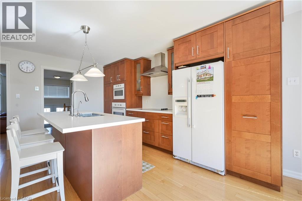 Kitchen featuring light wood-finish flooring, a central island with a white countertop and integrated sink, stainless steel faucet, and extensive wood cabinetry - 12 Langevin Drive, Wasaga Beach, ON