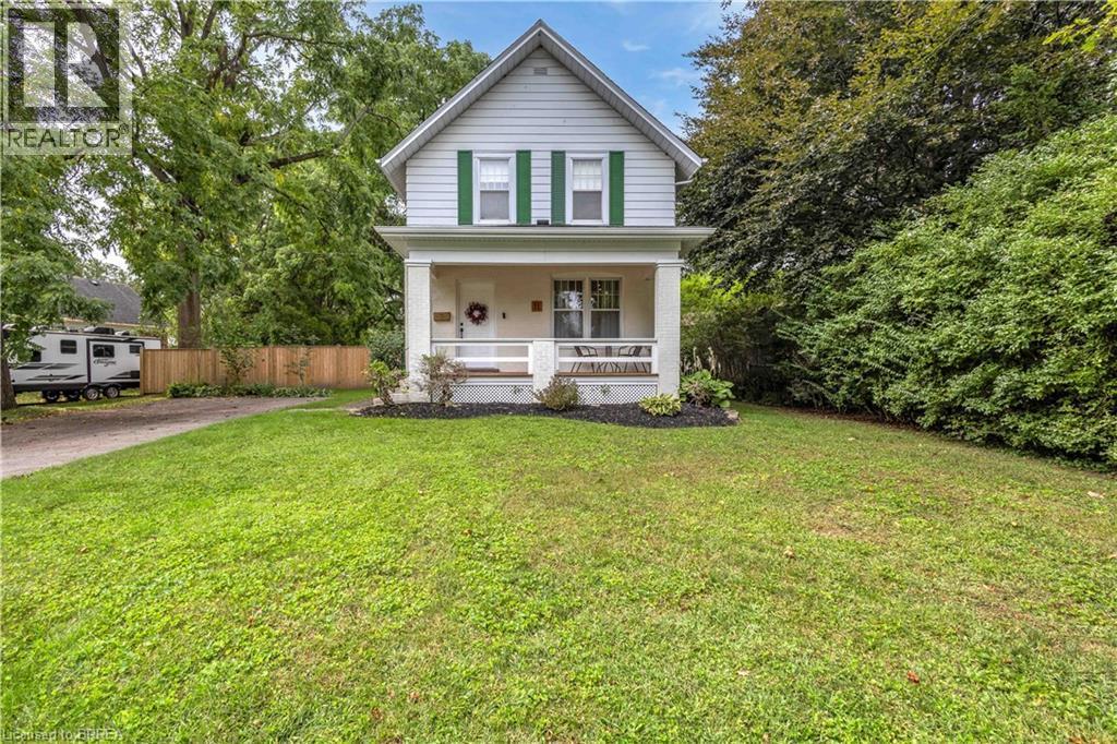 Pitched roofline residence with a covered front porch, featuring green window shutters and a surrounding privacy hedge - 11 Tutela Heights Road, Brantford, ON