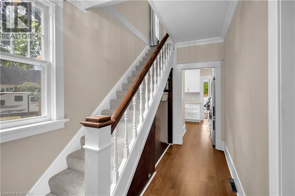 Hardwood flooring, carpeted staircase, white newel post with wood-finish cap, white window trim, and crown molding - 11 Tutela Heights Road, Brantford, ON