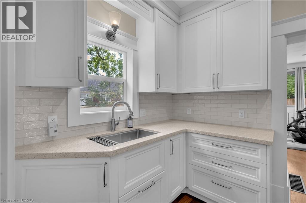 White cabinetry, light-toned countertops, subway tile backsplash, stainless steel sink, and a modern pull-down faucet - 11 Tutela Heights Road, Brantford, ON
