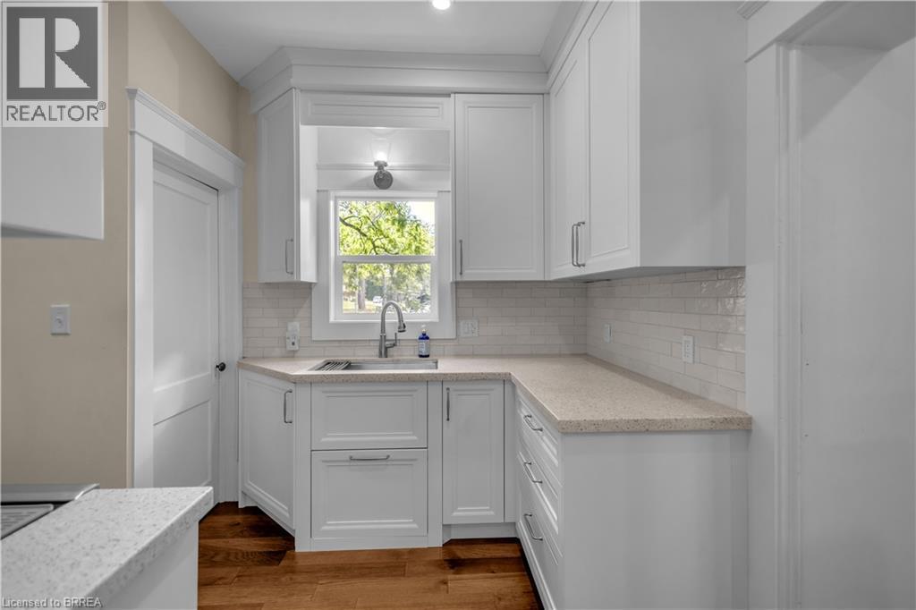 White shaker cabinetry, light-toned countertops, subway tile backsplash, stainless steel sink, and wood-finish flooring - 11 Tutela Heights Road, Brantford, ON