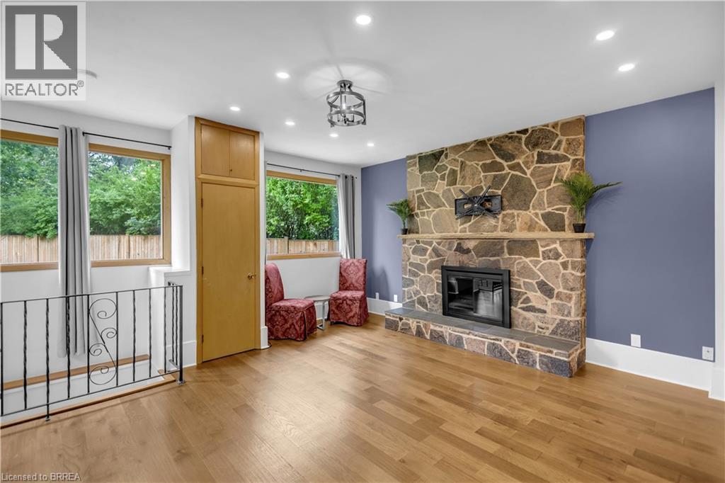 Stone fireplace with a hearth, wood-finish flooring, built-in cabinetry, recessed lighting, and a decorative ceiling fixture - 11 Tutela Heights Road, Brantford, ON