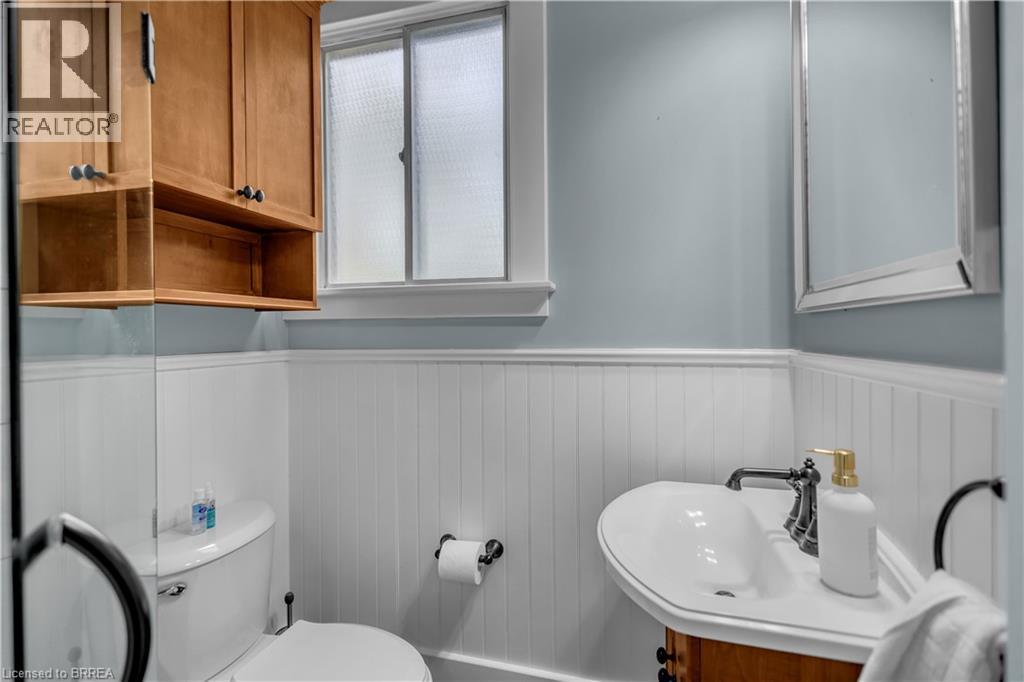 Pedestal sink, wood-finish vanity, wall-mounted mirror, wood-finish wall cabinet with open shelving, and white beadboard paneling - 11 Tutela Heights Road, Brantford, ON