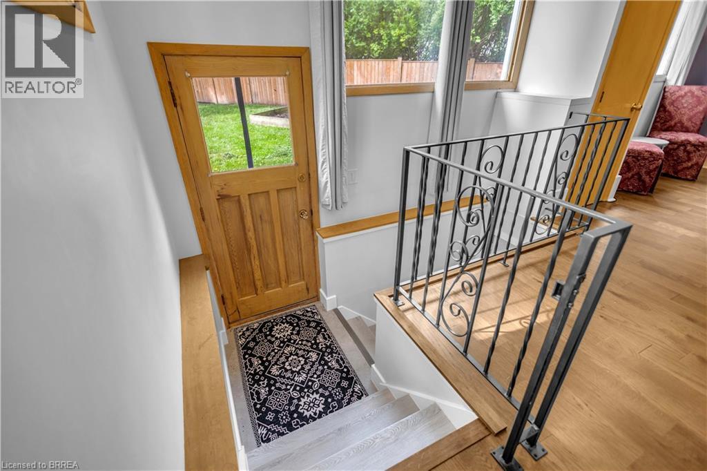 Hardwood flooring, painted white walls, wood-framed door with glass panel, wrought iron railing with scrollwork, and a wooden handrail - 11 Tutela Heights Road, Brantford, ON
