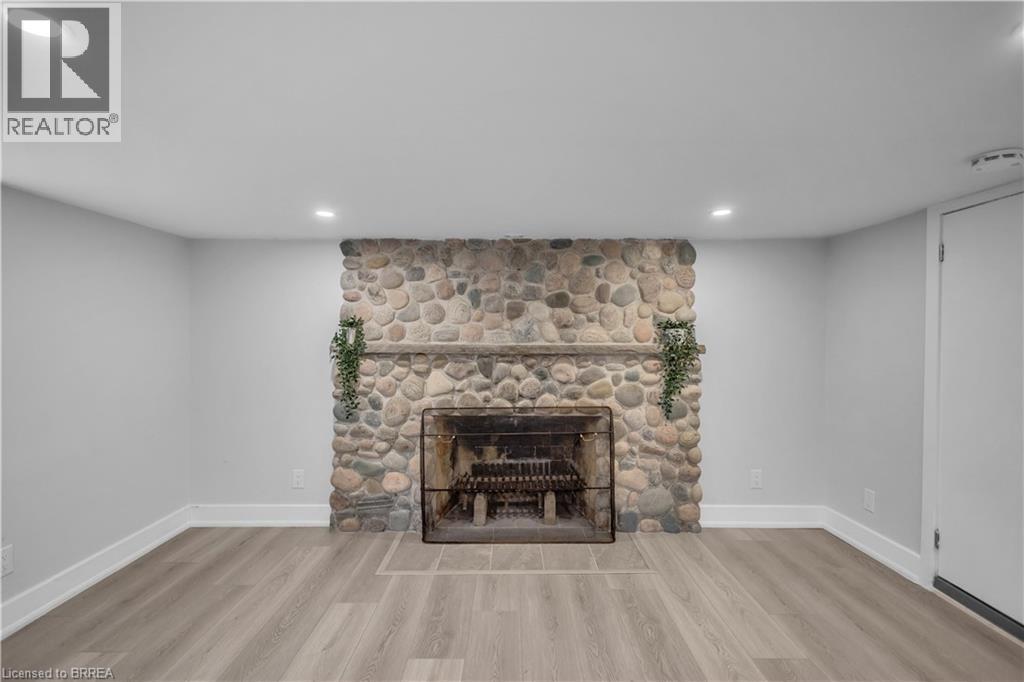 Stone-clad fireplace with hearth, wood-finish flooring, recessed lighting, and a white interior door - 11 Tutela Heights Road, Brantford, ON