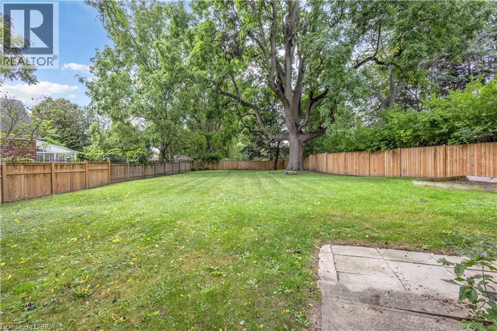 Expansive backyard featuring a manicured lawn, mature trees, and privacy fencing - 11 Tutela Heights Road, Brantford, ON