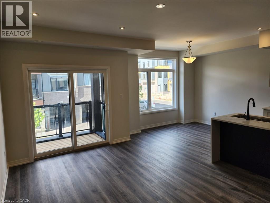 Spacious living area featuring wood-finish flooring, recessed lighting, and a sliding glass door opening to a private balcony with black metal railings - 155 Equestrian Way Unit# 152, Cambridge, ON