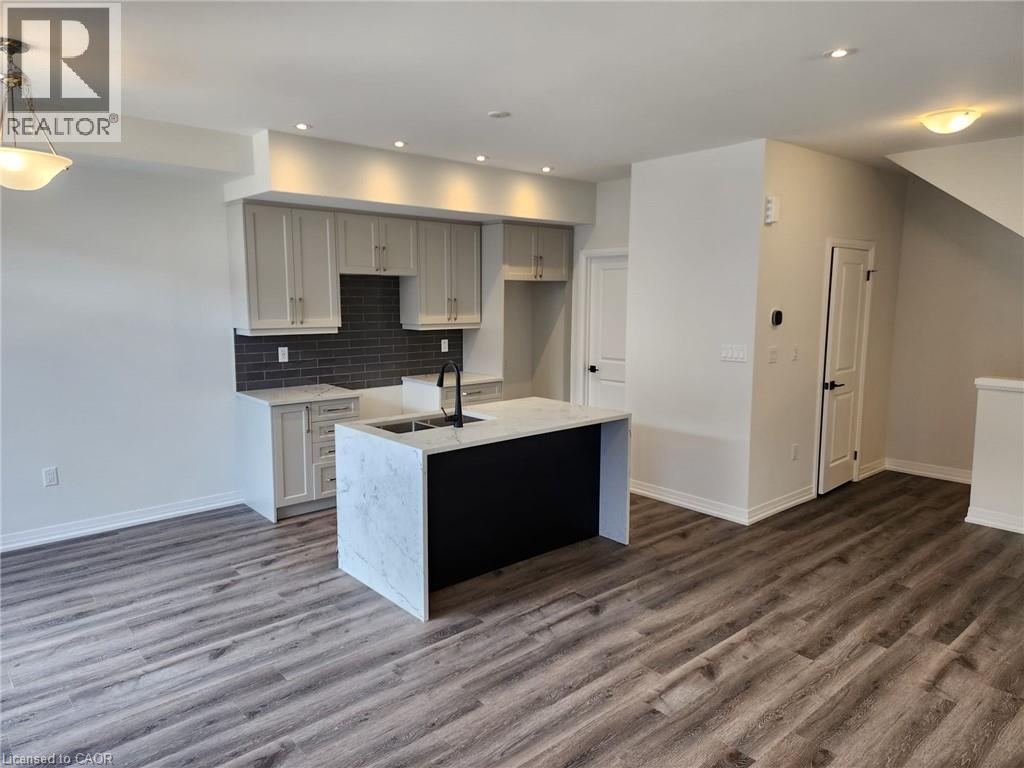 Contemporary kitchen island with a stone finish countertop and integrated sink, recessed lighting, wood-finish flooring, light cabinetry, and dark subway tile backsplash - 155 Equestrian Way Unit# 152, Cambridge, ON