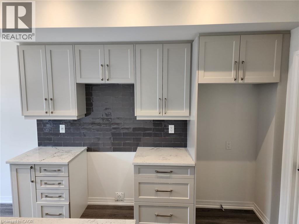 White shaker-style cabinetry, white countertops with subtle veining, dark subway tile backsplash, and dark wood-finish flooring - 155 Equestrian Way Unit# 152, Cambridge, ON