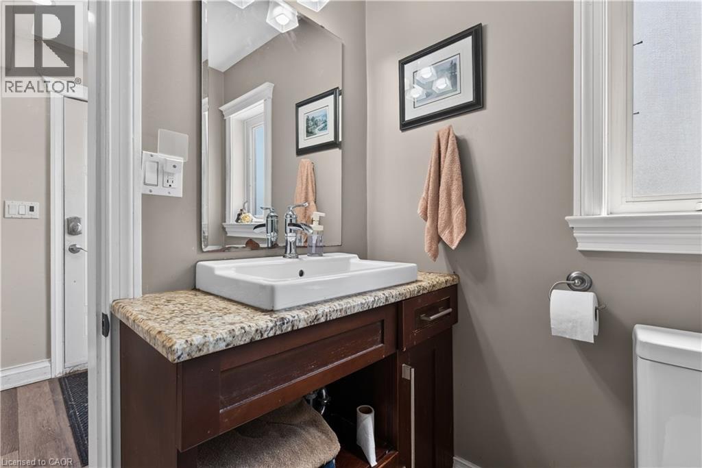 Bathroom featuring a vessel sink, stone countertop, dark wood-finish vanity, wall-mounted mirror, and a window with privacy glass - 42841 Highway 3, Wainfleet, ON