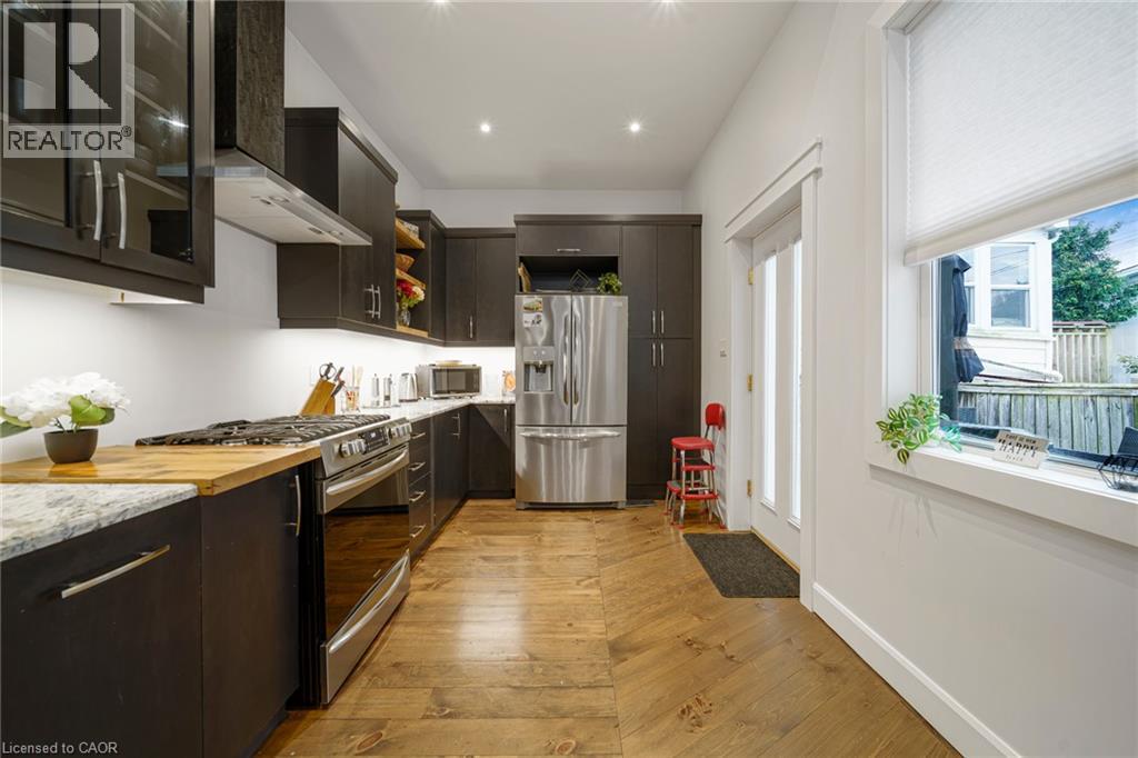 Galley kitchen with wood-finish flooring, stainless steel appliances, dark cabinetry, light countertops, and recessed lighting - 28 Cambridge Street, Cambridge, ON