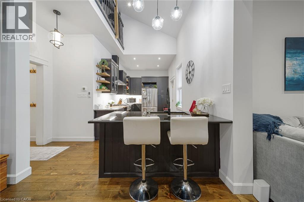Vaulted ceiling with pendant lighting, wood-finish flooring, dark wood cabinetry, built-in shelving, and a kitchen island with counter seating - 28 Cambridge Street, Cambridge, ON