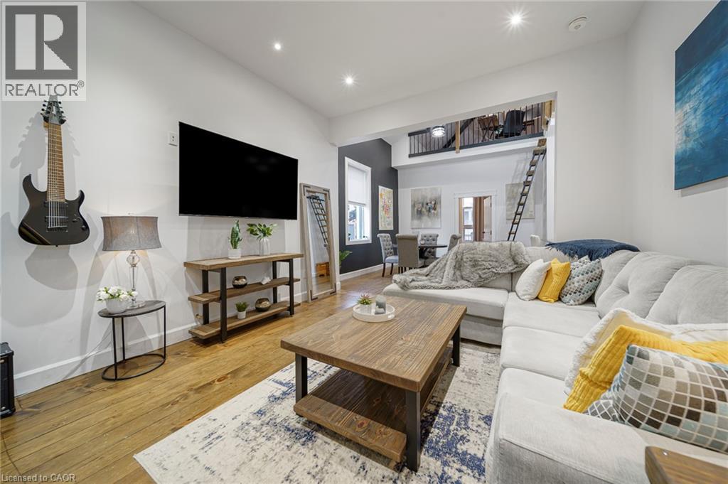 Recessed lighting illuminates the living space, featuring wood-finish flooring and a partial loft with a black railing - 28 Cambridge Street, Cambridge, ON