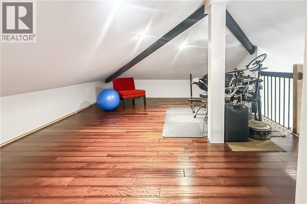 Sloped ceiling architecture with exposed beams, wood-finish flooring, and a white baluster railing - 28 Cambridge Street, Cambridge, ON