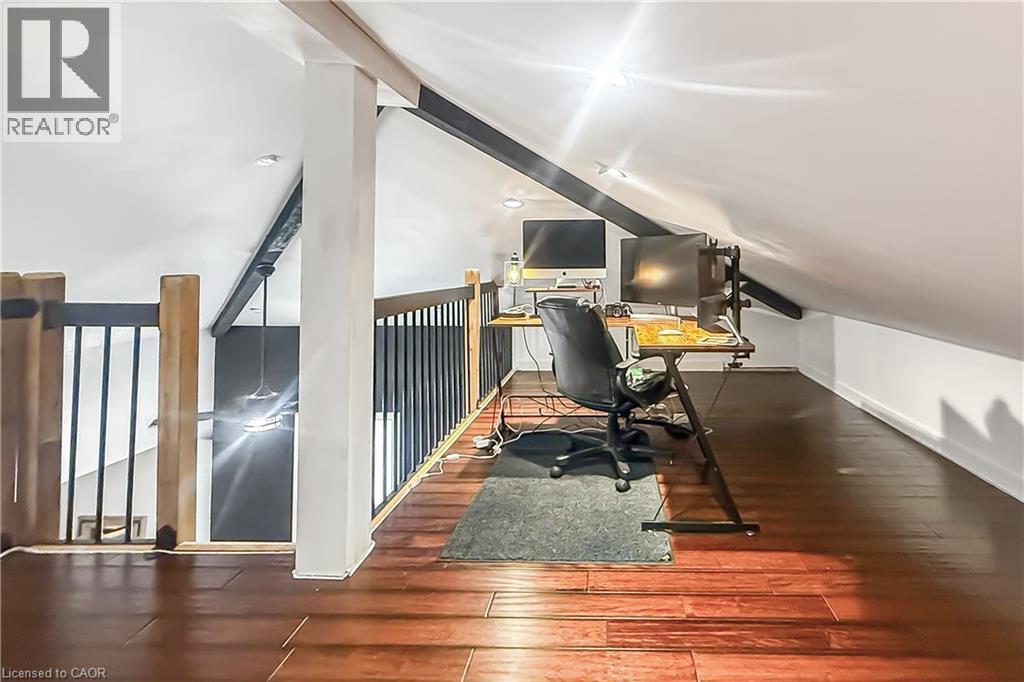 Attic loft space featuring wood-finish flooring, white vaulted ceilings, recessed lighting, and a wood and metal railing - 28 Cambridge Street, Cambridge, ON