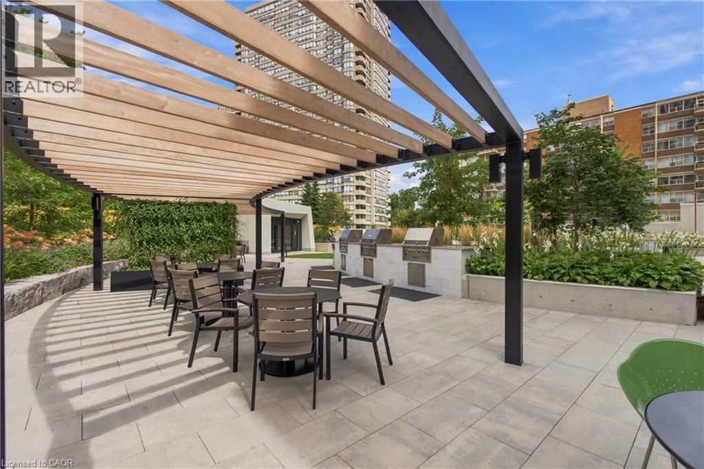 Curved wooden pergola with black metal frame, paver patio, built-in BBQ stations, and a lush green wall - 60 Central Park Roadway Unit# 2010, Etobicoke, ON