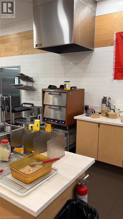 Stainless steel commercial-grade exhaust hood, white subway tile backsplash, wood-finish wall panels, light wood-finish cabinetry, dark flooring - 105 City Centre Drive Unit# 1, Mississauga, ON