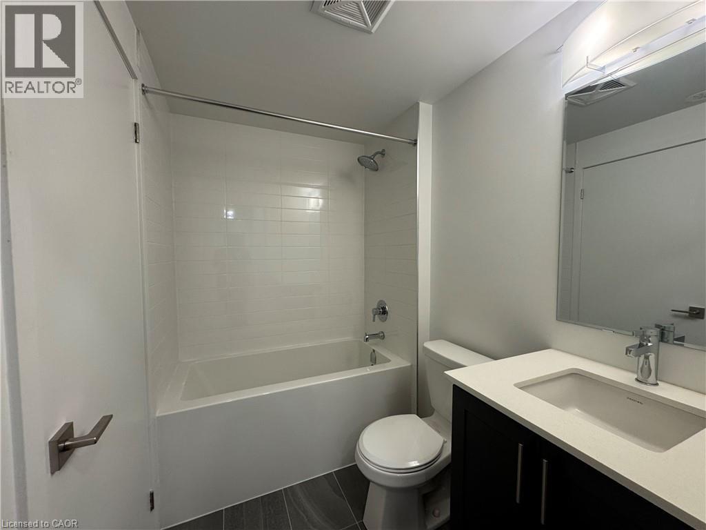 Full-size bathtub with a subway tile surround, dark wood-finish vanity with a light countertop, and a wall-mounted mirror with integrated lighting - 17 Lytham Green Circle Unit# 27, Newmarket, ON