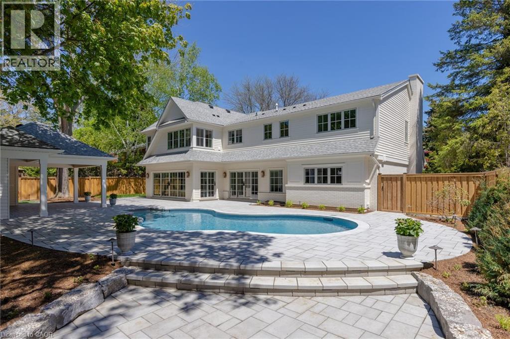 White exterior residence featuring a curved swimming pool, extensive paver patio, stone retaining wall, and a covered outdoor pavilion - 130 Edgecliffe Place, Halton, ON