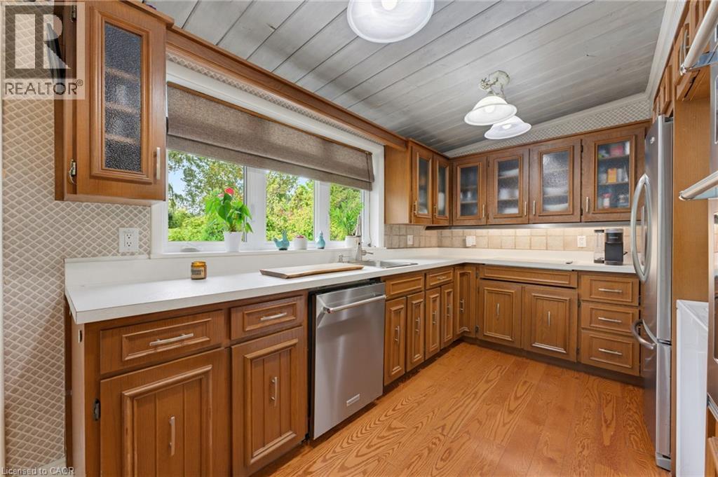 Wood-finish cabinetry with glass panel doors, white countertops, tile backsplash, and stainless steel appliances - 1316 Nevarc Drive, Burlington, ON