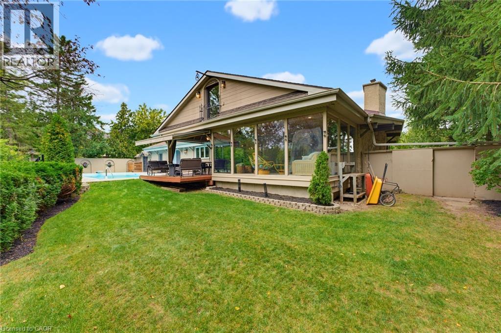 Manicured lawn, elevated wood deck, expansive sunroom with large windows, exterior chimney, and an in-ground pool - 1316 Nevarc Drive, Burlington, ON