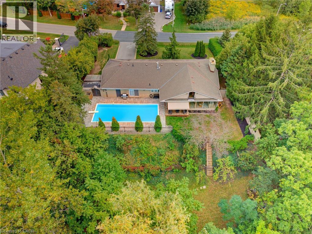 In-ground swimming pool, sunroom, mature trees, landscaped grounds, and a sloped backyard with terraced steps - 1316 Nevarc Drive, Burlington, ON